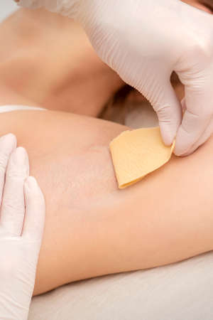 Close up of hands in gloves of beautician waxing young female armpit with sugar paste in hair...