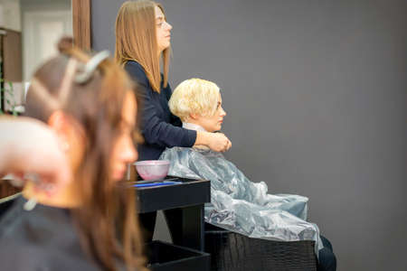 The female hairdresser puts on a transparent cellophane cape to the female client in a beauty hair...