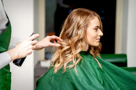 Side view of female hairdresser using hairspray fixing clients female hair in a hair salonの写真素材