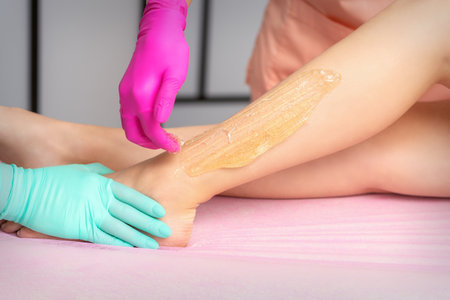 Two female cosmetologists waxing womans legs with hot sugar paste in a beauty spa salonの写真素材