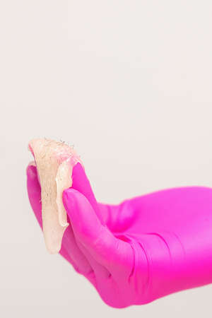 Close up of the hand of a beautician in pink glove holding white sugar paste with removed hair against a white backgroundの写真素材
