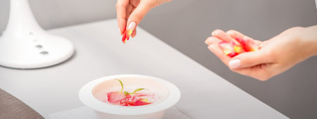 Beauticians female hands preparing manicure bath with red and pink roses petals on the table in spaの写真素材