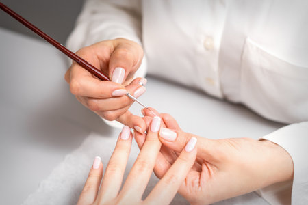 French manicure. Manicure master drawing white varnish on the nail tip with a thin brush, close upの写真素材