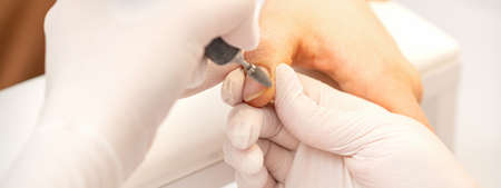Manicure master applying electric nail file machine removing old nail polish on fingernails in a nail salonの写真素材