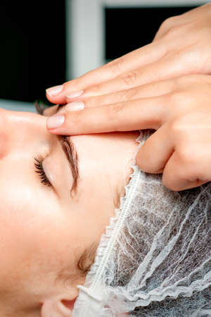 Side view fingers of female therapist making anti-age massage of forehead wrinkles to young caucasian woman in spa beauty salonの写真素材