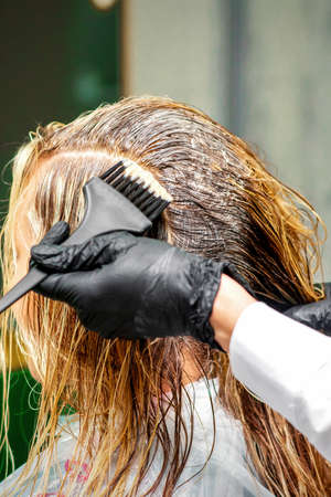 Hand of a hairdresser in black gloves applying dye to the female hair in a beauty salonの写真素材
