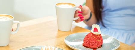 Two young women with cups of coffee and pieces of cake sitting at the table in a cafe outdoors