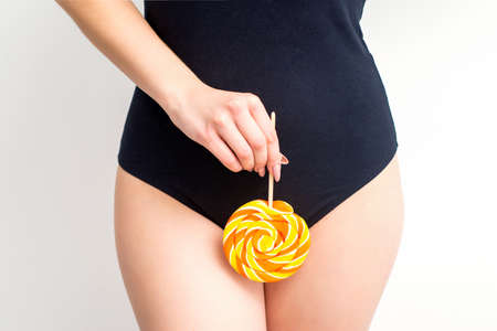 Woman holding lollipop candy on bikini zone, the concept of intimate depilation, problems of...