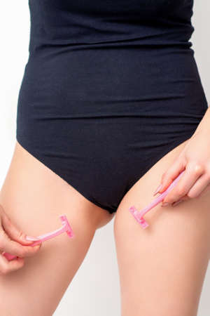 Young woman shaving crotch in bikini zone with two razors standing on white background, concept skincare and hair removalの写真素材