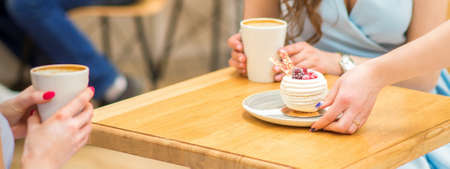 The waitresss hand puts the piece of cupcake on the table at a cafe, woman hand is putting round little pastry on the table on a background of a female in a blue dressの写真素材