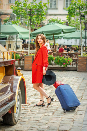Tourist business young woman in beautiful red jacket is pulling the suitcase on the city streetの写真素材