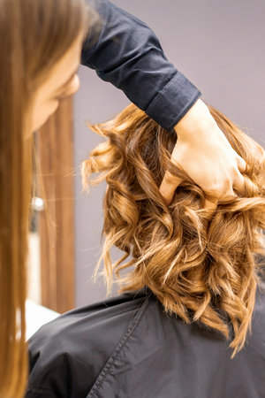Female hairdresser checks brown curly hairstyle of a young caucasian woman in beauty salonの写真素材