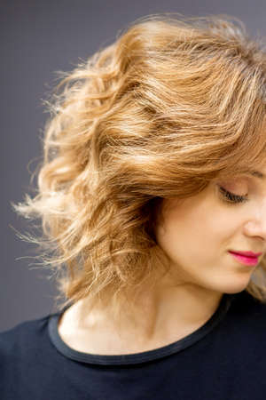 Beautiful young caucasian woman with a red short curly hairstyle looking down on dark backgroundの写真素材
