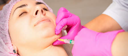 The cosmetologist makes lipolytic injection on the chin of a young woman against the double chin in a beauty salonの写真素材