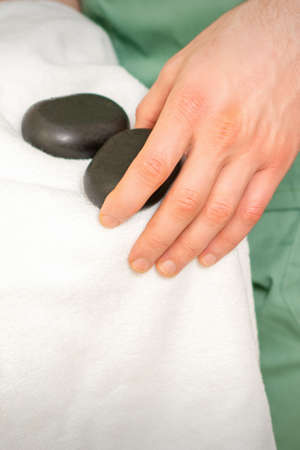 Close up of masseurs hand wipes black massage stones with a white towel