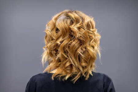 Back view of the woman with long brown curly hair stands on a dark backgroundの写真素材