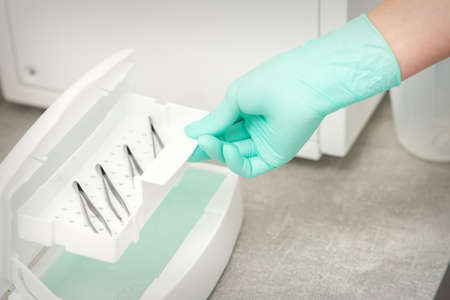 The beautician holds a tray of tweezers preparing them for disinfection with a special liquid and...