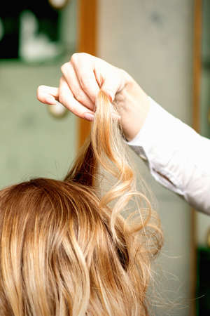 Female coiffeur fixing hairstyling of blonde woman with hairspray in a beauty salonの写真素材