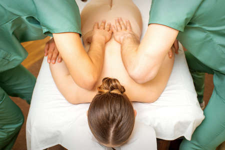 Back and hands double massage with four hands of two professional massagers for a young caucasian woman in a spa salonの写真素材