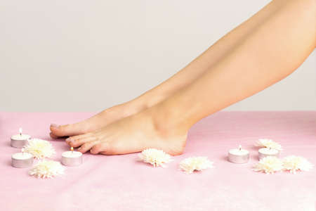 Beautiful white smooth feet of young woman with candles and flowers on pink couchの写真素材