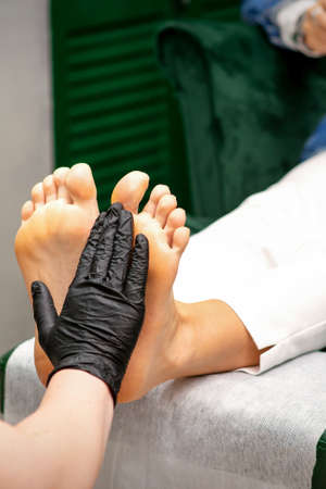 Moisturizing the feet. Hands of pedicure master in black gloves care about female feet. Foot massage. Pedicure beauty salon conceptの写真素材