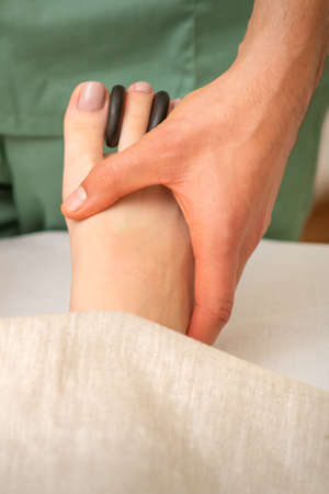Massager doing feet and toes massage with rocks between a female toesの写真素材