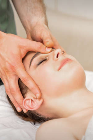 Pretty young caucasian woman receiving a head massage by a male massage therapist in a beauty salonの写真素材