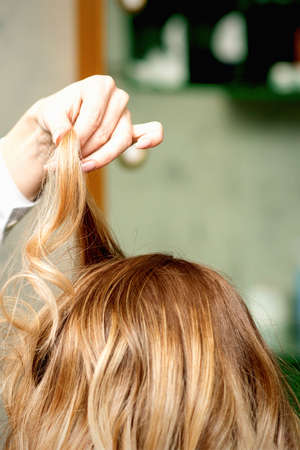 Female coiffeur fixing hairstyling of blonde woman with hairspray in a beauty salonの写真素材