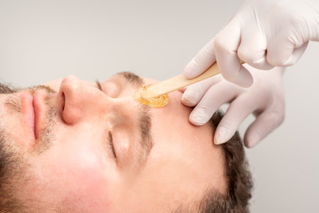 Beautician applying wax paste between eyebrows during the procedure of waxing in the beauty salonの写真素材