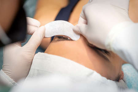 The beautician is gluing a patch under her eyes, before the procedure of eyelash extension. Artificial extended eyelashesの写真素材