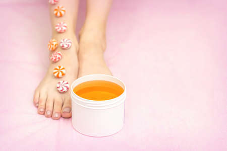 Round candies lying in a row on female feet with white jar with sugar paste on pink background with copy space, depilation conceptの写真素材