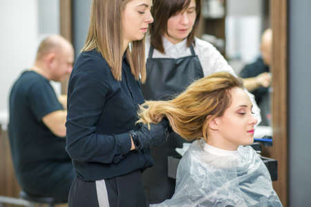 Two female hairstylists prepare long hair of a young woman making curls hairstyle in a beauty salonの写真素材