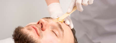 Beautician applying wax paste between eyebrows during the procedure of waxing in the beauty salonの写真素材