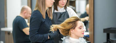 Two female hairstylists prepare long hair of a young woman making curls hairstyle in a beauty salonの写真素材
