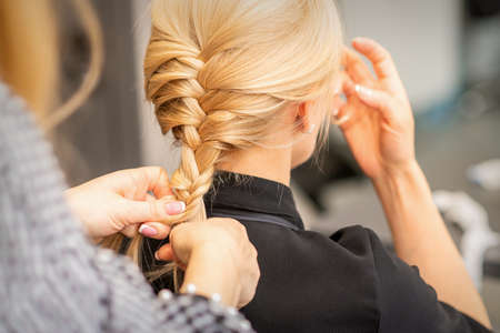 Braiding braid. Hands of female hairdresser braids long braid for a blonde woman in a hair salonの写真素材