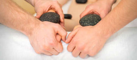 Two masseurs make a foot massage with a hot stone in four hands at the spa
