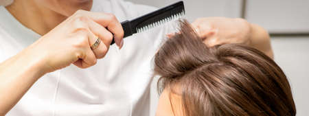 Professional hairdresser doing hairstyle for a beautiful brunette young woman with long hair. Concept of fashion and beautyの写真素材