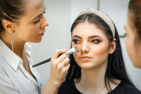 Closeup portrait of a woman applying dry cosmetic tonal foundation on the face using a makeup brush. Makeup detailの写真素材