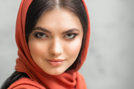 Portrait of a pretty young caucasian woman with makeup in a red headscarf on gray backgroundの写真素材