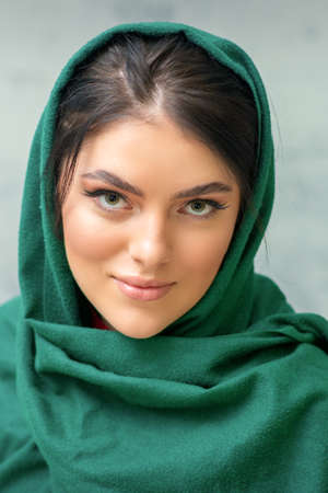 Portrait of a pretty young caucasian woman with makeup in a green headscarf on gray backgroundの写真素材