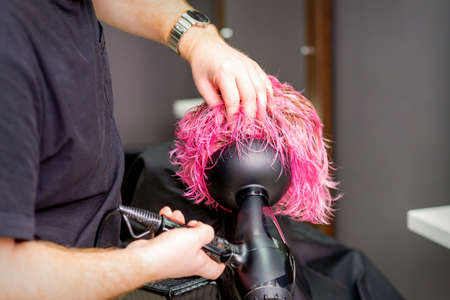 Hair Stylist making hairstyle using hair dryer blowing on wet custom pink hair at a beauty salonの写真素材