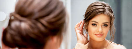 Beautiful young caucasian woman looking at her new haircut in the mirror touches hairstyle