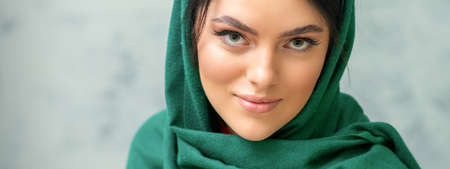 Portrait of a pretty young caucasian woman with makeup in a green headscarf on gray backgroundの写真素材