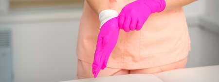 Hand of beautician puts on sterile pink gloves prepares to receive clients indoorsの写真素材