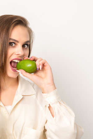 Diet nutrition. Beautiful young caucasian woman biting organic green avocado on white background....