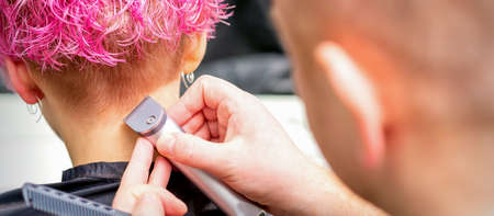 Hairdresser shaving nape and neck with electric trimmer of a young caucasian woman with short pink hair in a beauty salonの写真素材