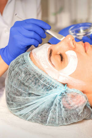 Face peeling at the beautician. Facial treatment. The beautician applies a cleansing face mask to...