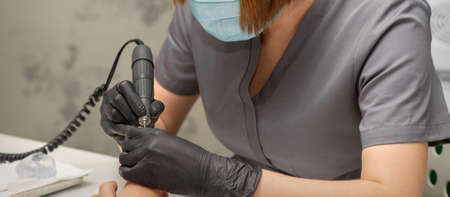 Manicurist removes nail polish uses the electric machine of the nail file during manicure in a nail...