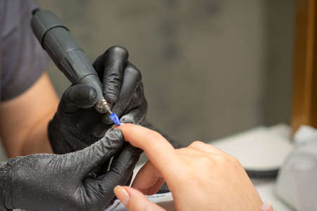 Manicurist removes nail polish uses the electric machine of the nail file during manicure in a nail salonの写真素材