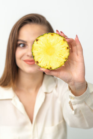 A young attractive pretty nice caucasian smiling woman holds ring slice pineapple covering her eye against a white background. Healthy eating conceptの写真素材